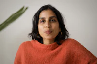 a woman in an orange sweater is standing in front of a plant