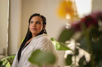 a woman in a white robe sitting in front of flowers
