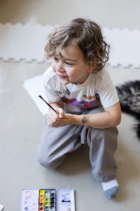 a young boy sitting on the floor with a paint brush
