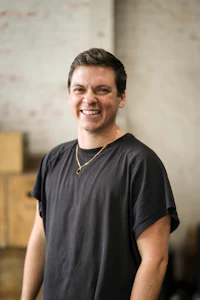 a smiling man in a black shirt standing in a warehouse