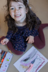 a little girl sitting on the floor with a paint brush