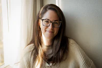 a woman in glasses leaning against a window