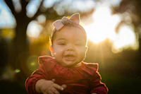 a baby girl in a red dress smiles at the sun