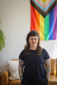 a woman with tattoos standing in front of a rainbow flag