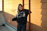 a woman leaning against a wall wearing a black sweatshirt