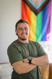 a man in a green shirt standing in front of a rainbow flag