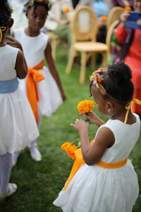 a group of little girls wearing white dresses and orange flowers
